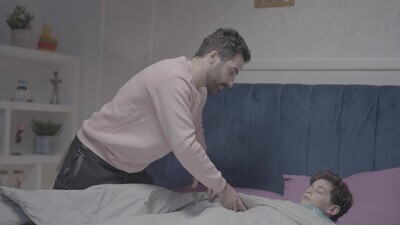 a father carrying his boy and putting him in bed
