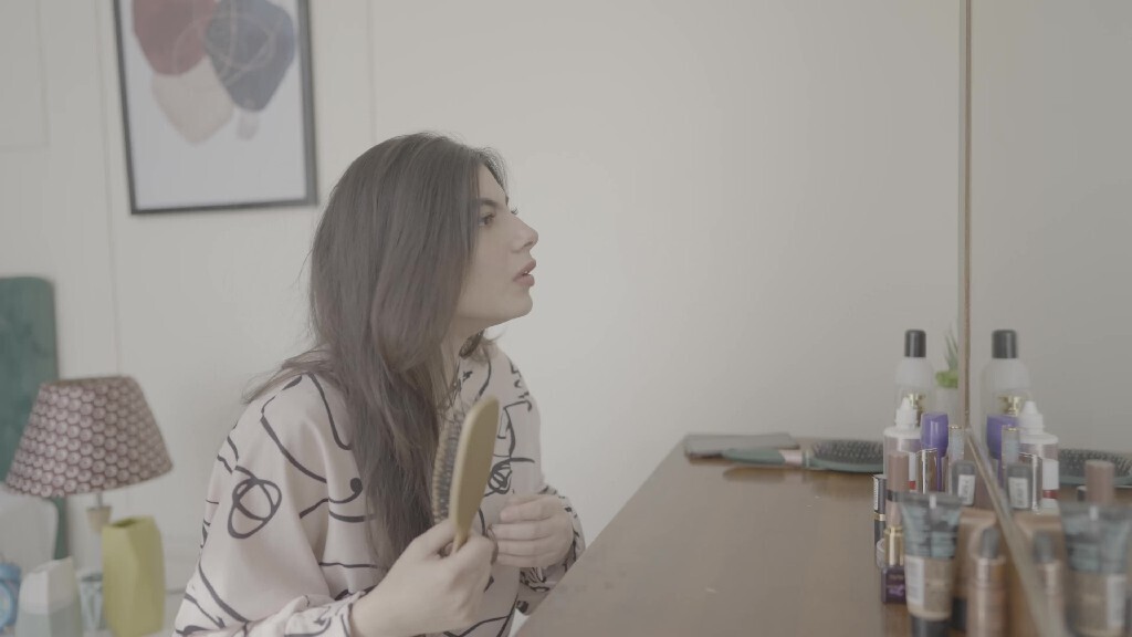 a woman sitting in front of the mirror brushing her hair