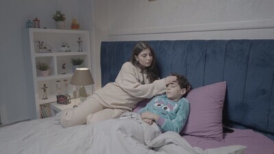 امراة تجلس على السرير تقيس درجة حرارة طفلها 