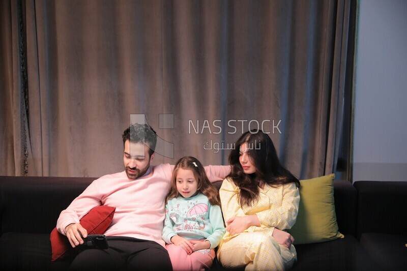 a family of three sitting on the sofa and watching television