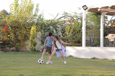 a brother playing football with his sister in the garden