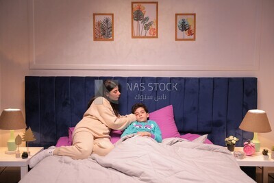 a woman sitting in bed takes her son&#39;s temperature