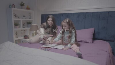 a mother with her daughter drawing together on the bed