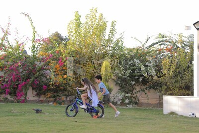 a girl riding a bike and her brother running with her in the garden