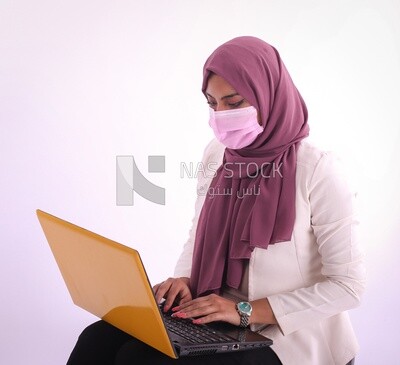 امراة بحجاب ترتدى كمامة زهرية تعمل على اللاب توب