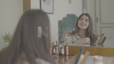 a woman sitting in front of the mirror brushing her hair
