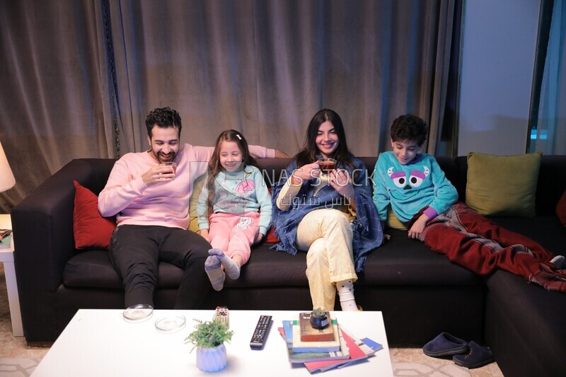 a family of four sitting on the sofa laughing and drinking a cup of tea