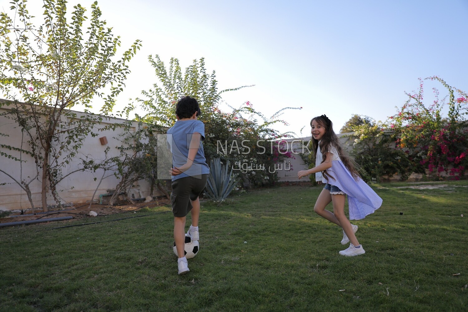 a brother playing football with his sister in the garden
