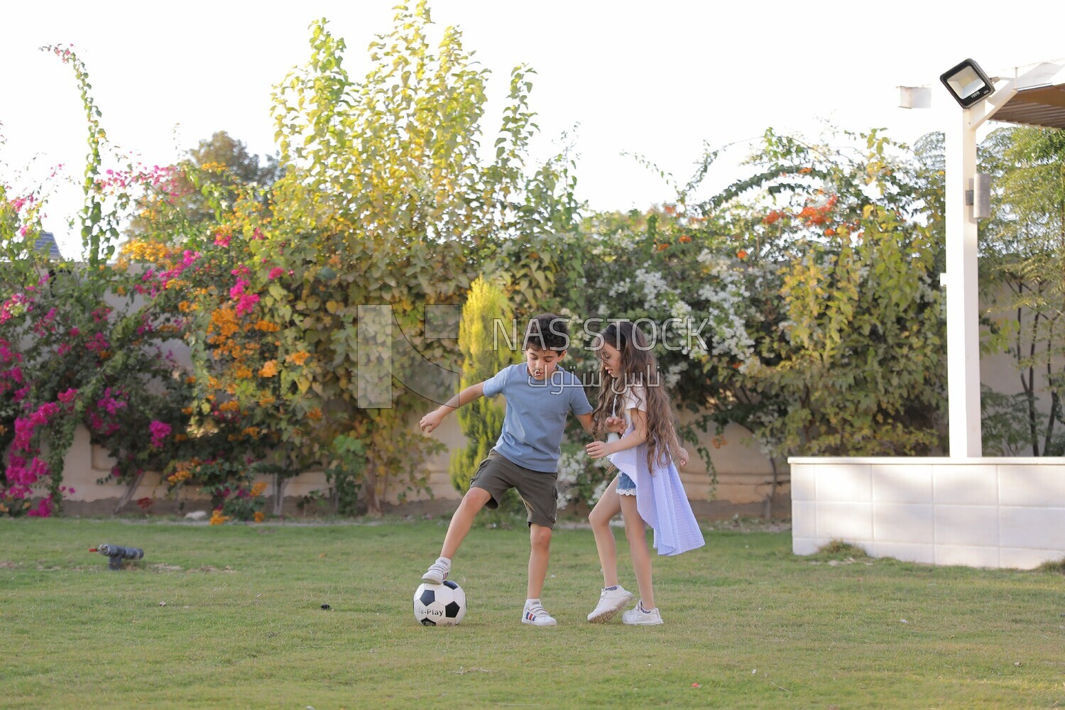 a brother playing football with his sister in the garden