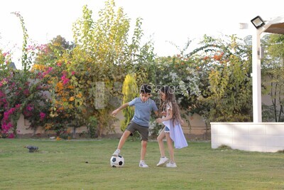 a brother playing football with his sister in the garden