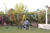 a girl riding a bike and her brother running with her in the garden