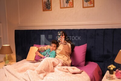 a woman reading a story to her child and taking a selfie in bed