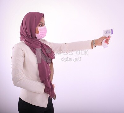 امراة بحجاب ترتدى كمامة زهرية تعمل على اللاب توب