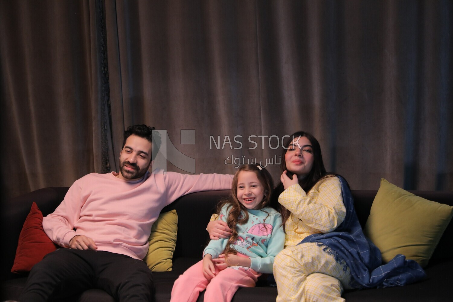 a family of three sitting on the sofa and watching television