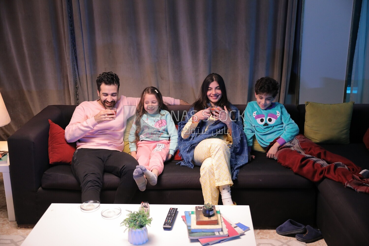a family of four sitting on the sofa laughing and drinking a cup of tea