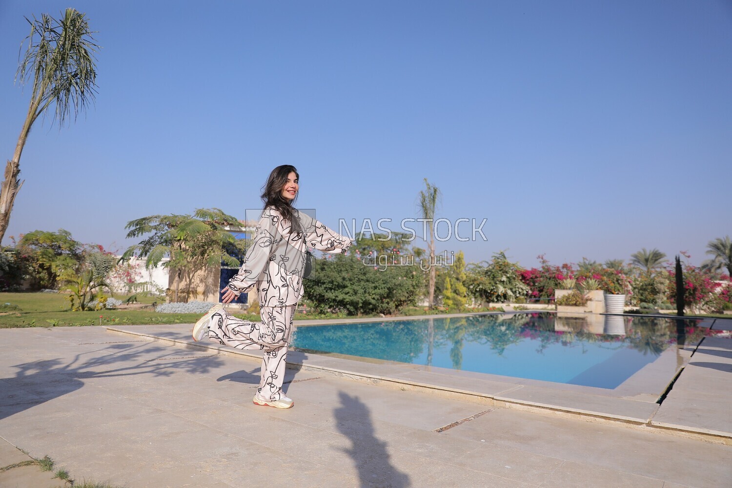 a woman standing in the garden beside a swimming pool