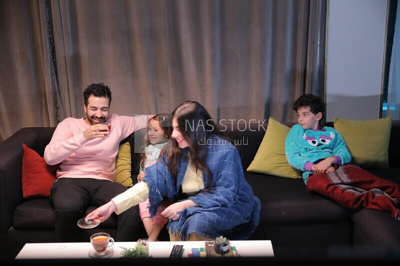 a family of four sitting on the sofa laughing and drinking a cup of tea