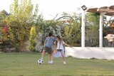 a brother playing football with his sister in the garden