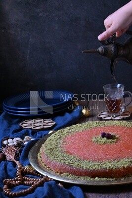 Plate of palestine knafeh with some nuts on it next to a cup of tea