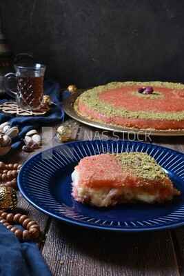 Plate of palestine knafeh with some nuts on it next to a cup of tea
