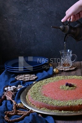 Plate of palestine knafeh with some nuts on it next to a cup of tea