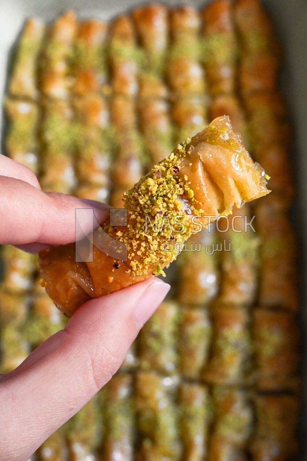 Hand holding a piece of egyptian sweet goulash with nuts on it