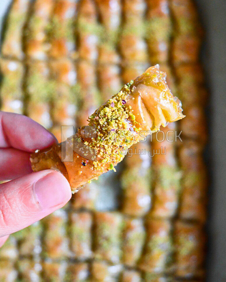 Hand holding a piece of egyptian sweet goulash with nuts on it