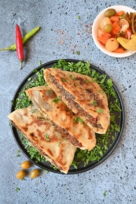 dish with hawawshi next to a spicy pepper and olive