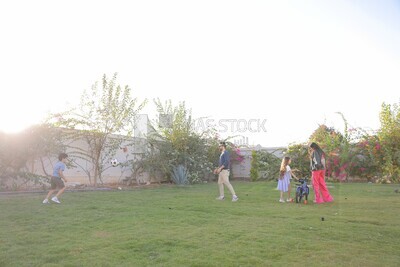 a father playing football with his son while the mother helps her daughter ride a bike in the garden