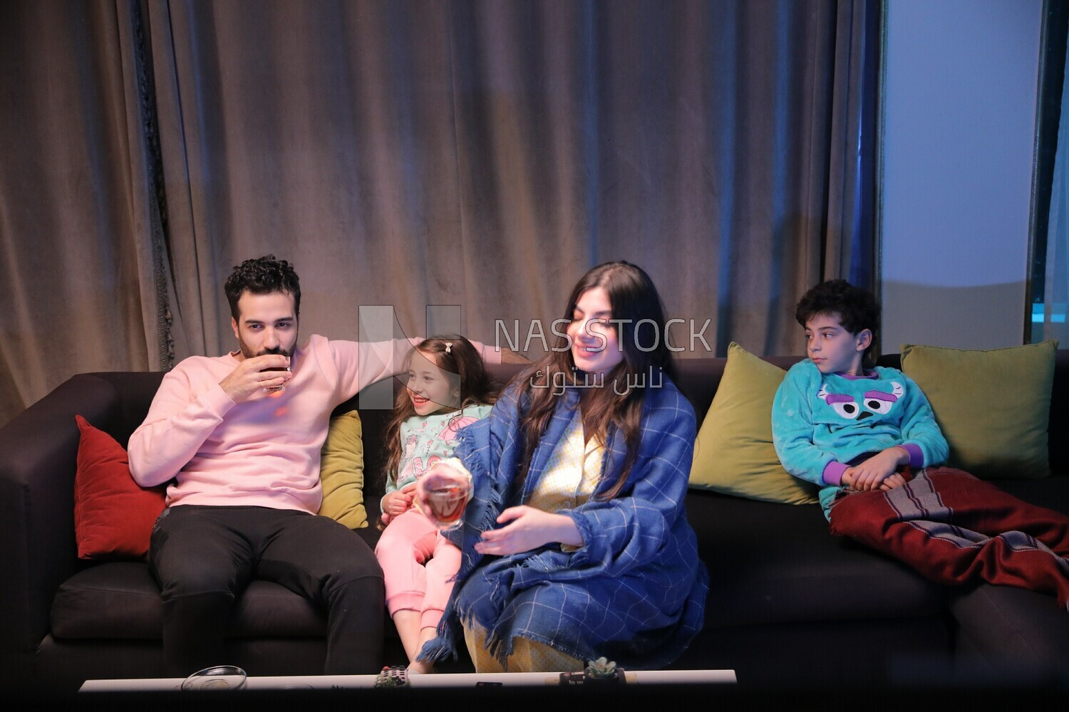 a family of four sitting on the sofa laughing and drinking a cup of tea
