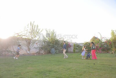 a father playing football with his son while the mother helps her daughter ride a bike in the garden