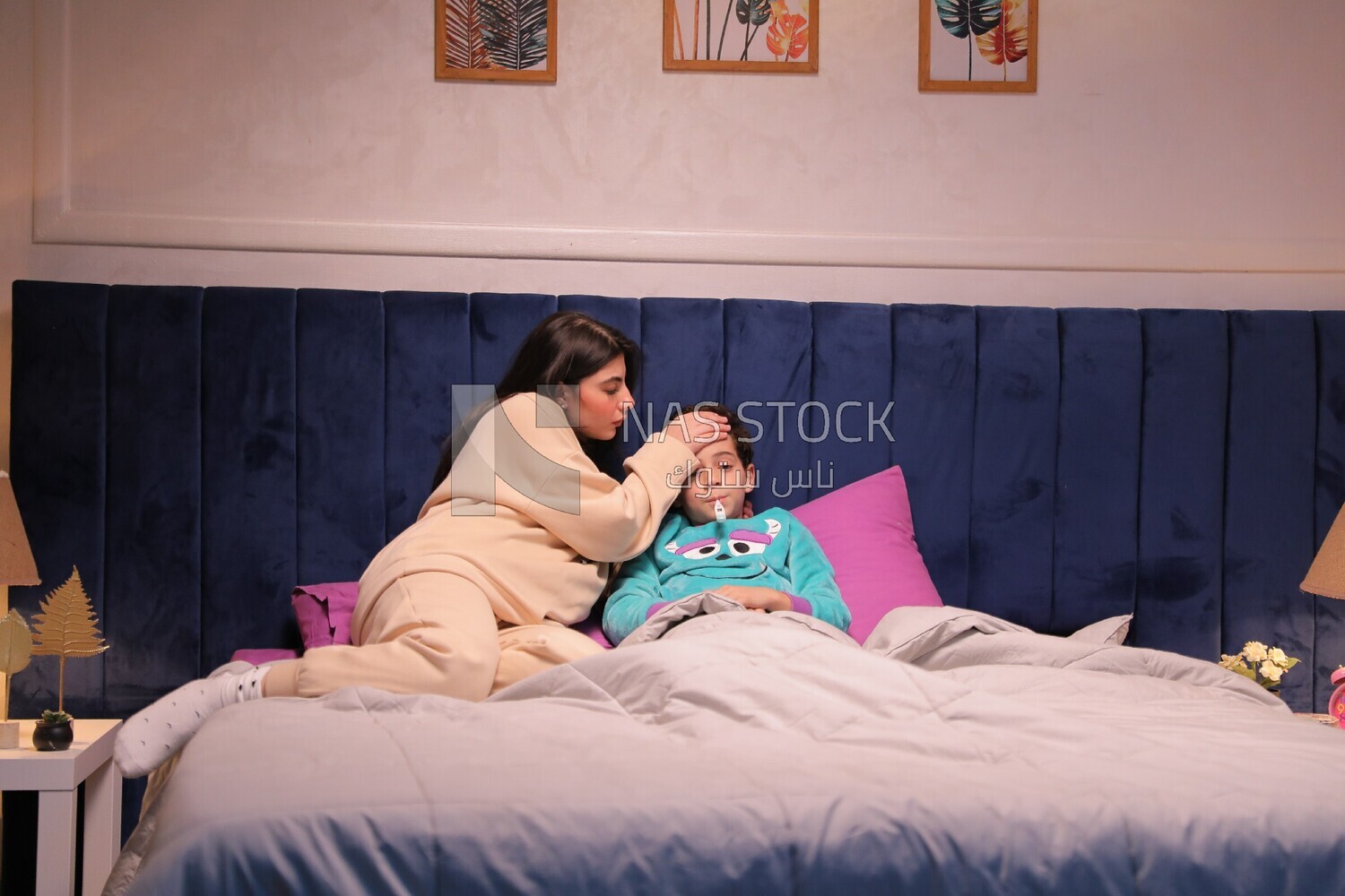 a woman sitting in bed takes her son&#39;s temperature