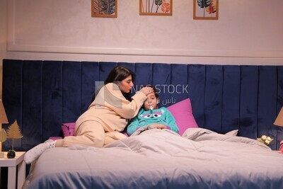 a woman sitting in bed takes her son&#39;s temperature