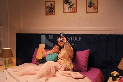 a woman reading a story to her child and taking a selfie in bed