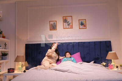 a woman sitting in bed takes her son&#39;s temperature