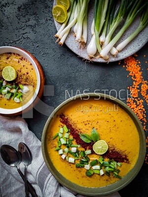 Plate of egyptian lentil soup with onion, lemon, and bread.