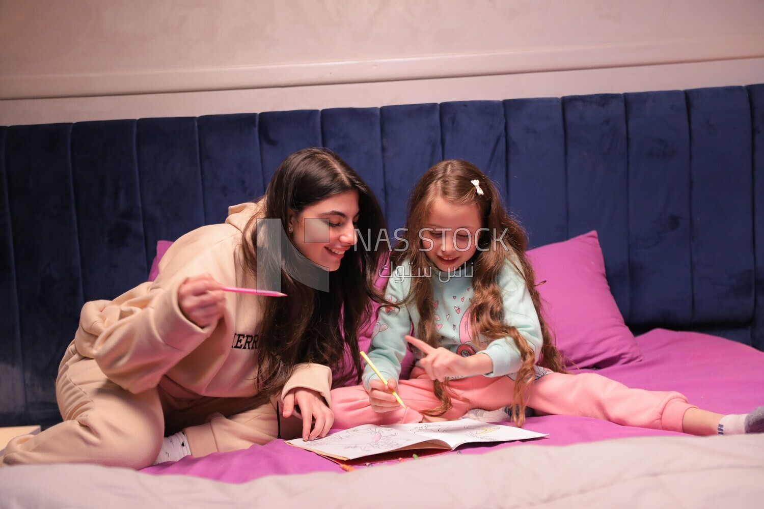 a mother with her daughter drawing together on the bed