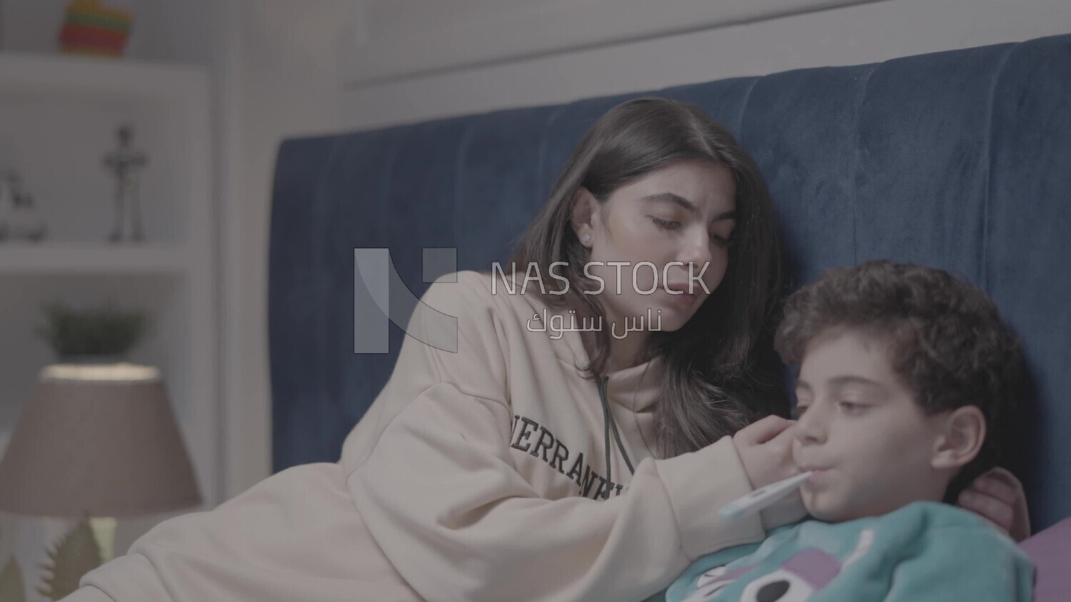 a woman sitting in bed takes her son&#39;s temperature