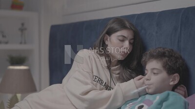 a woman sitting in bed takes her son&#39;s temperature