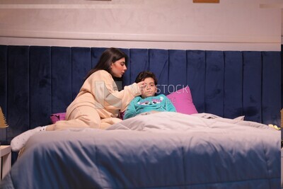 a woman sitting in bed takes her son&#39;s temperature