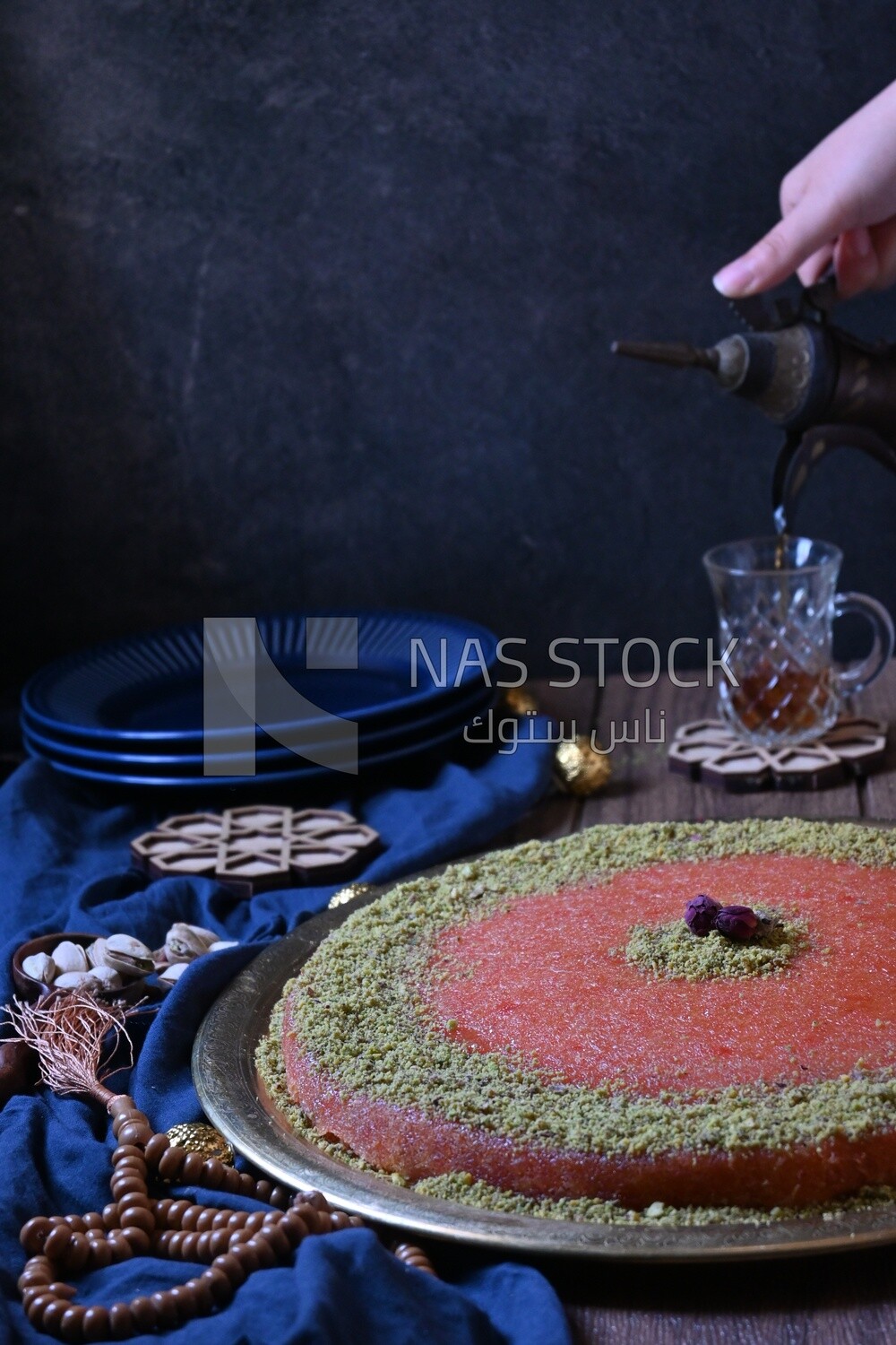 Plate of palestine knafeh with some nuts on it next to a cup of tea