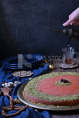 Plate of palestine knafeh with some nuts on it next to a cup of tea
