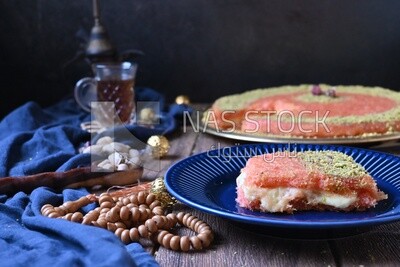 Plate of palestine knafeh with some nuts on it next to a cup of tea