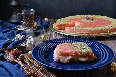 Plate of palestine knafeh with some nuts on it next to a cup of tea