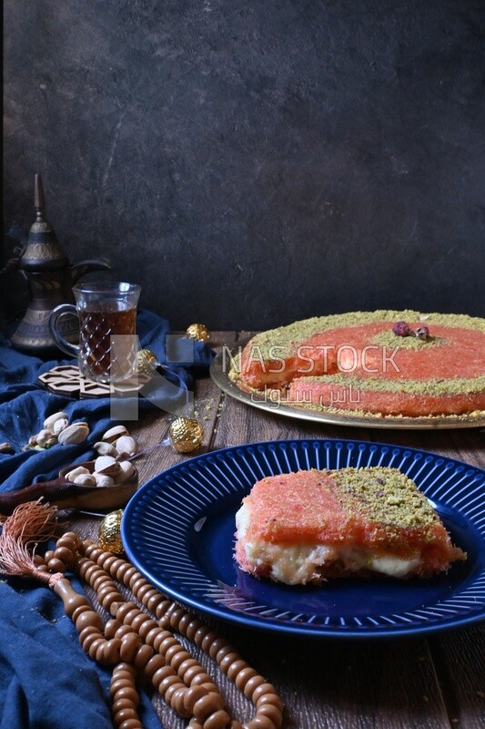Plate of palestine knafeh with some nuts on it next to a cup of tea