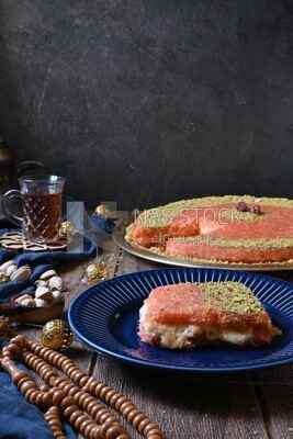 Plate of palestine knafeh with some nuts on it next to a cup of tea