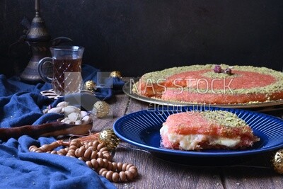Plate of palestine knafeh with some nuts on it next to a cup of tea