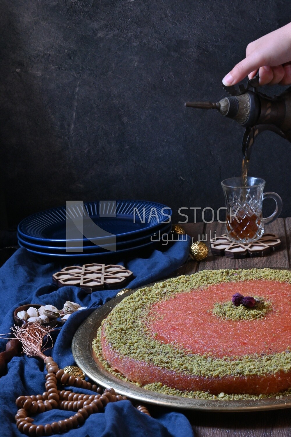 Plate of palestine knafeh with some nuts on it next to a cup of tea
