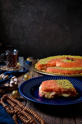 Plate of palestine knafeh with some nuts on it next to a cup of tea