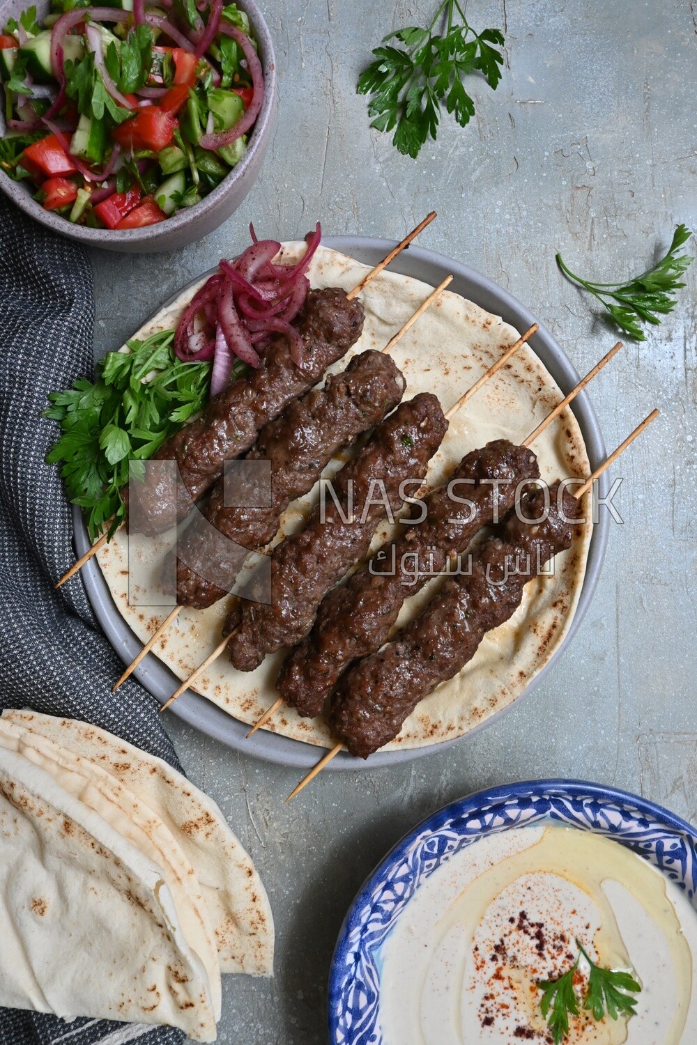 Dish with grilled kofta next to two plates of salads